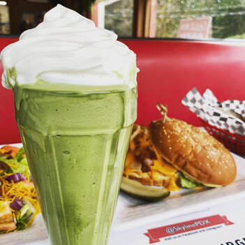 Dark green milshake with whipped cream burgers in the background